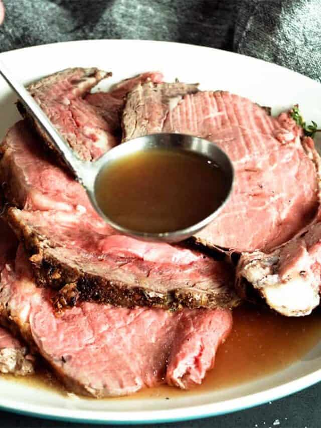 pouring au jus over sliced prime rib on a white plate