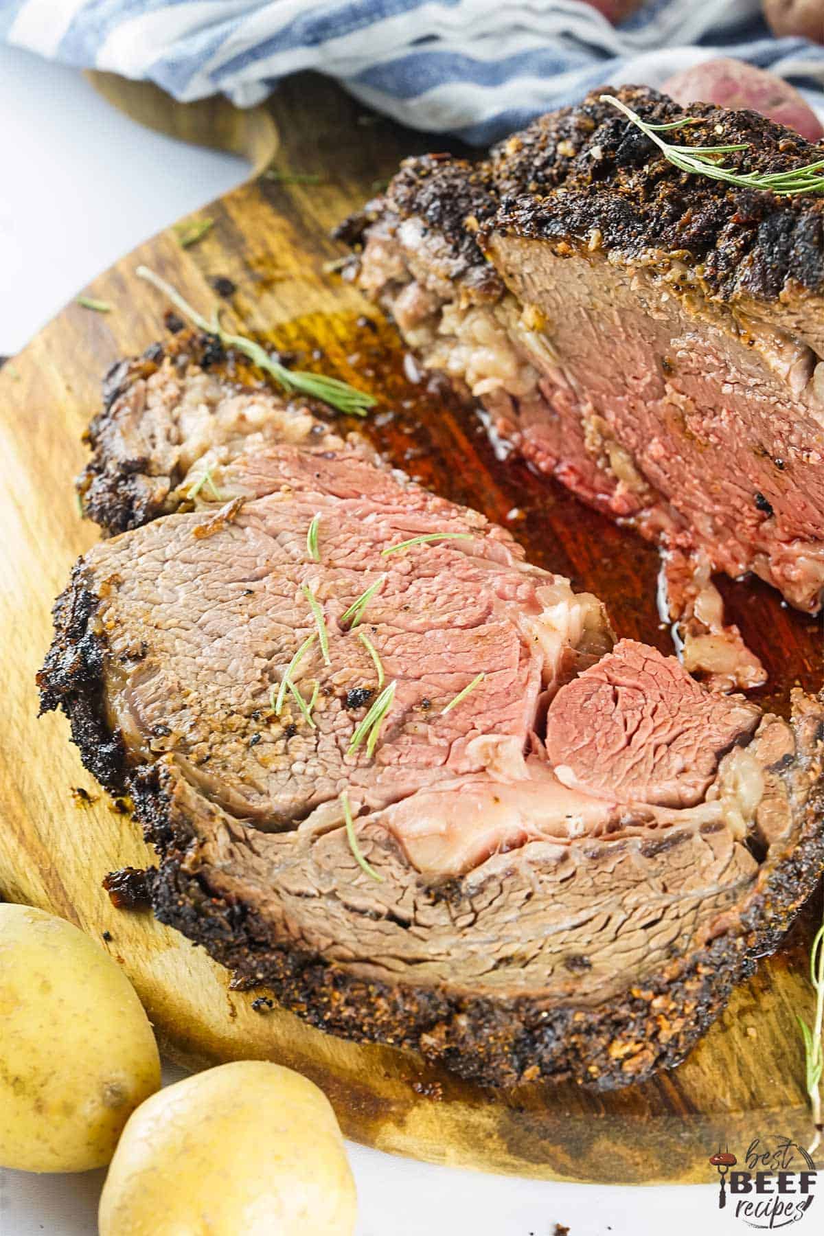 Sliced prime rib on a cutting board with potatoes and herbs