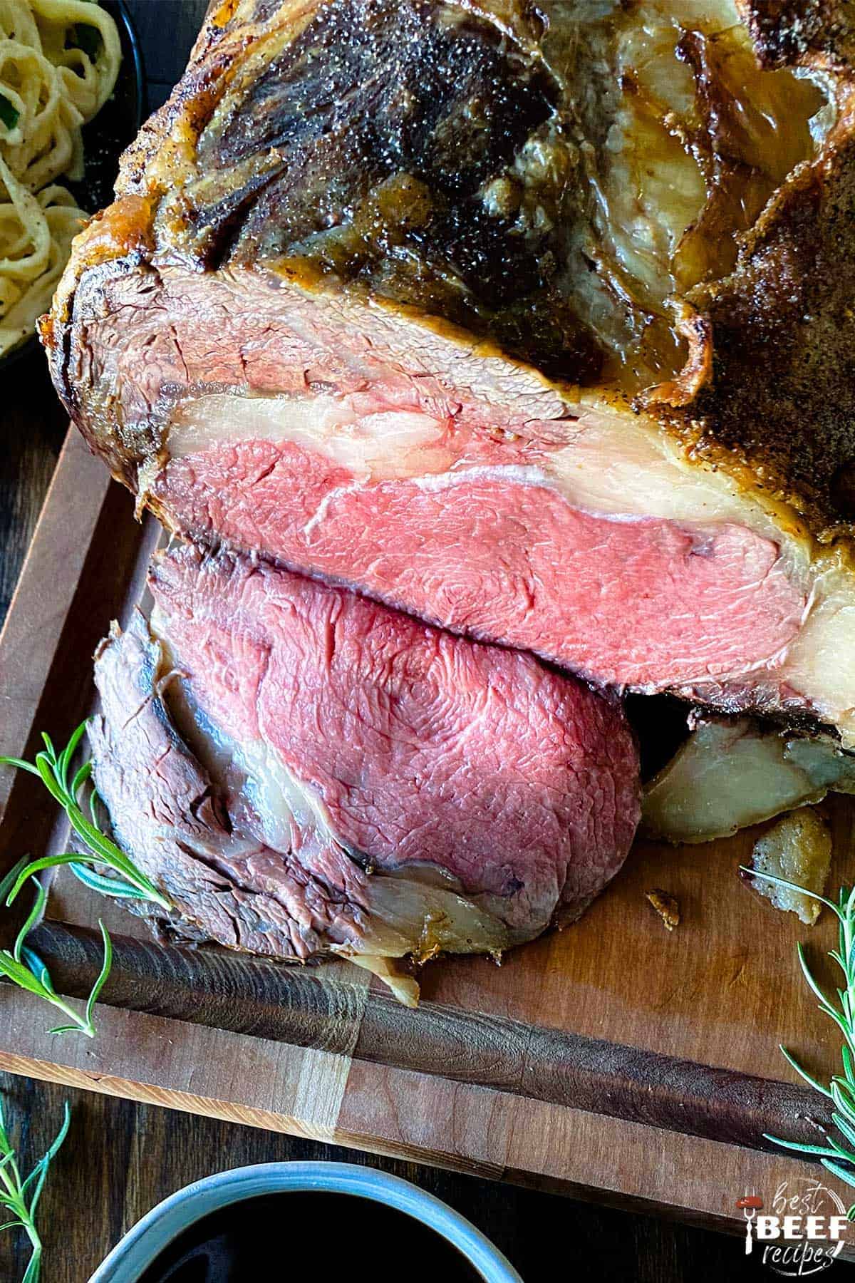 Sliced prime rib roast on a cutting board with herbs