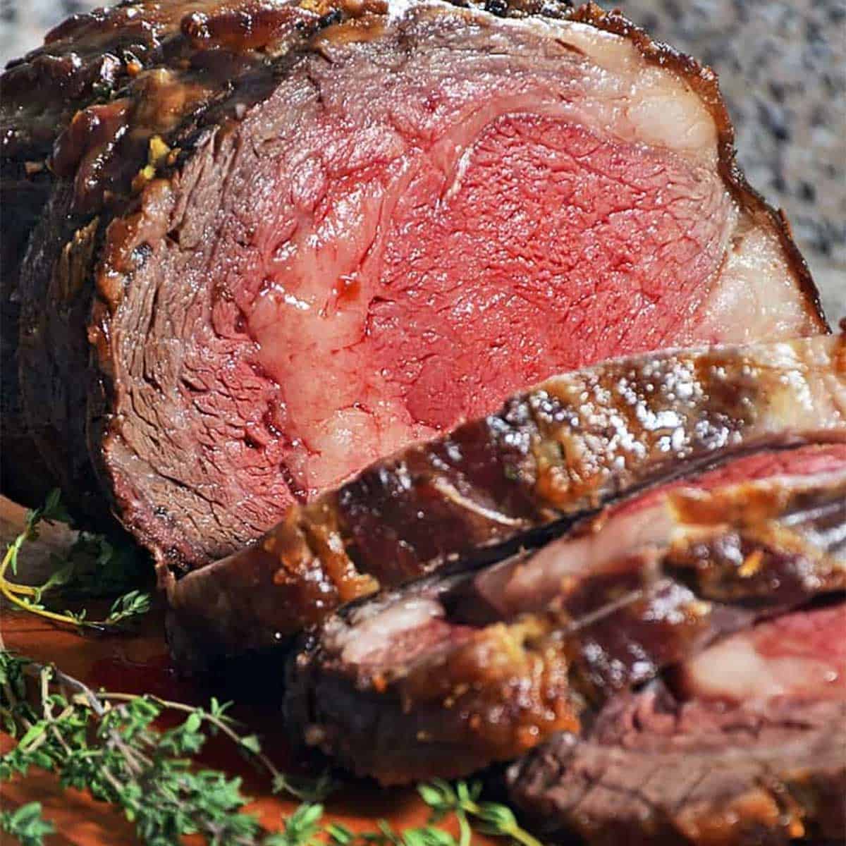 Slow roasted prime rib sliced on a cutting board with herbs