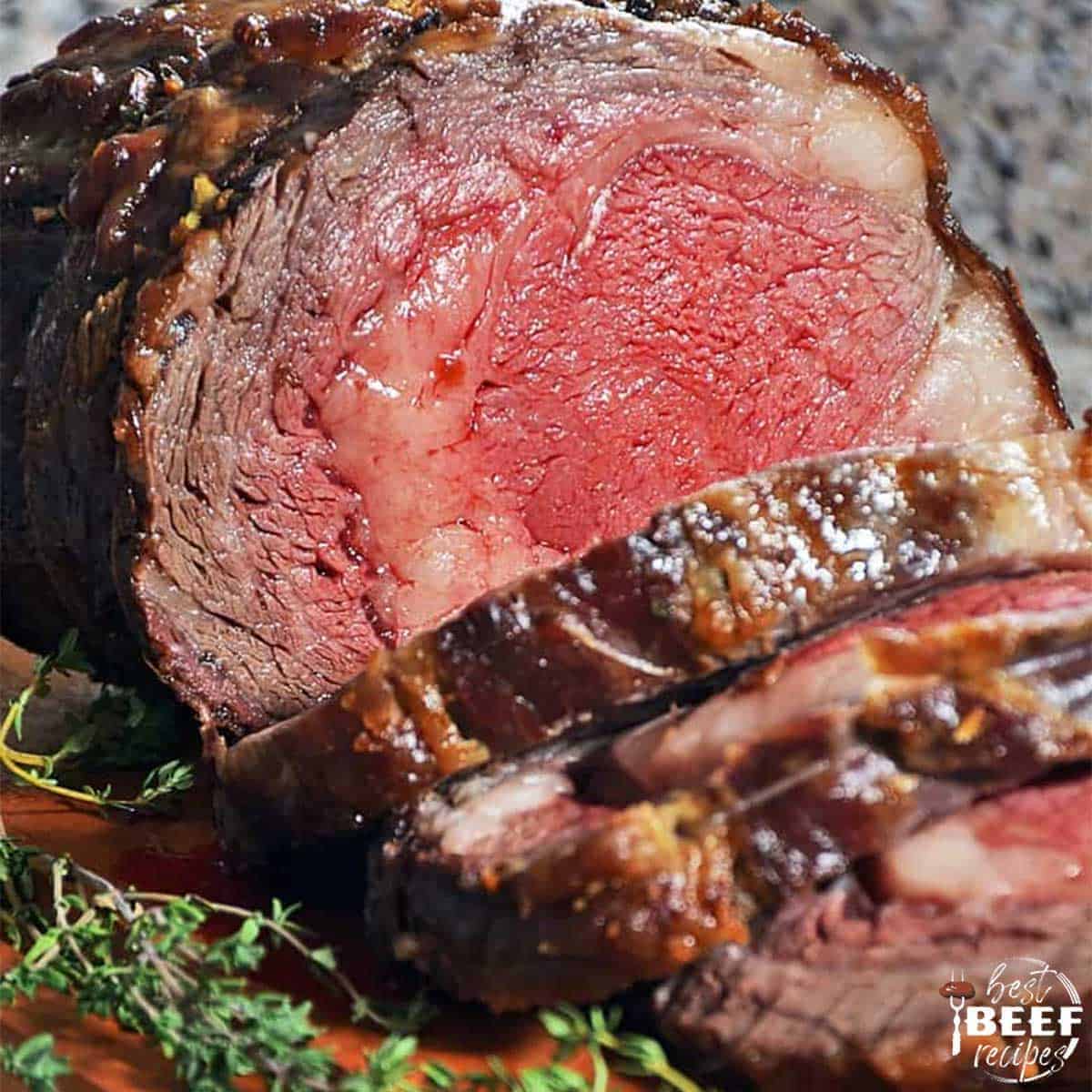 Slow roasted prime rib sliced on a cutting board with herbs