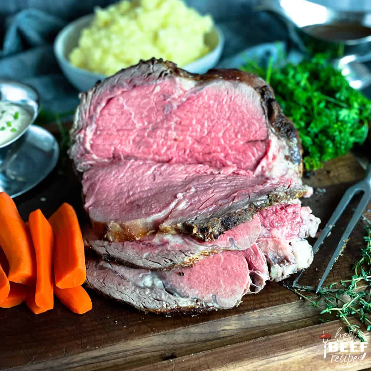 Sous vide prime rib sliced on a cutting board next to carrots and greens