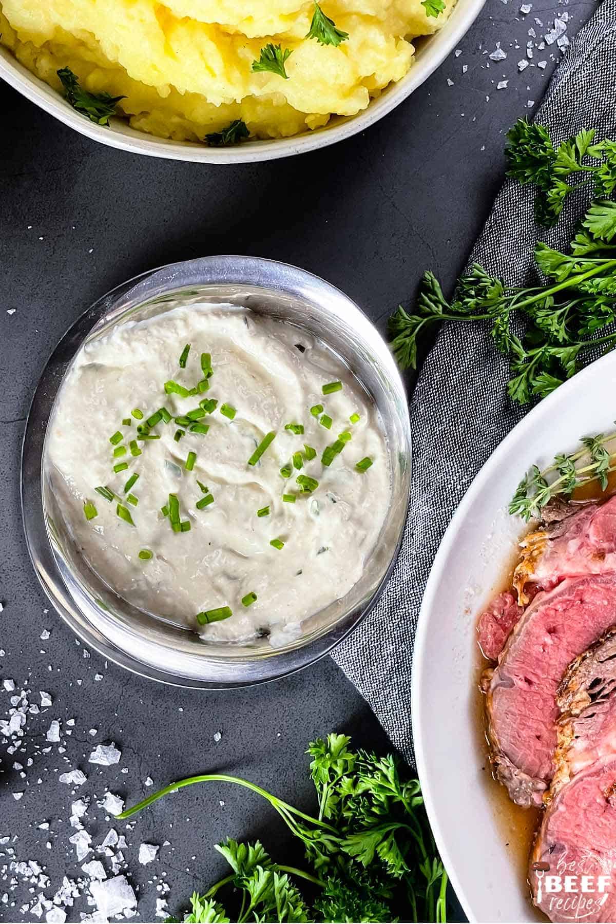 horseradish sauce in a silver bowl next to plate of prime rib