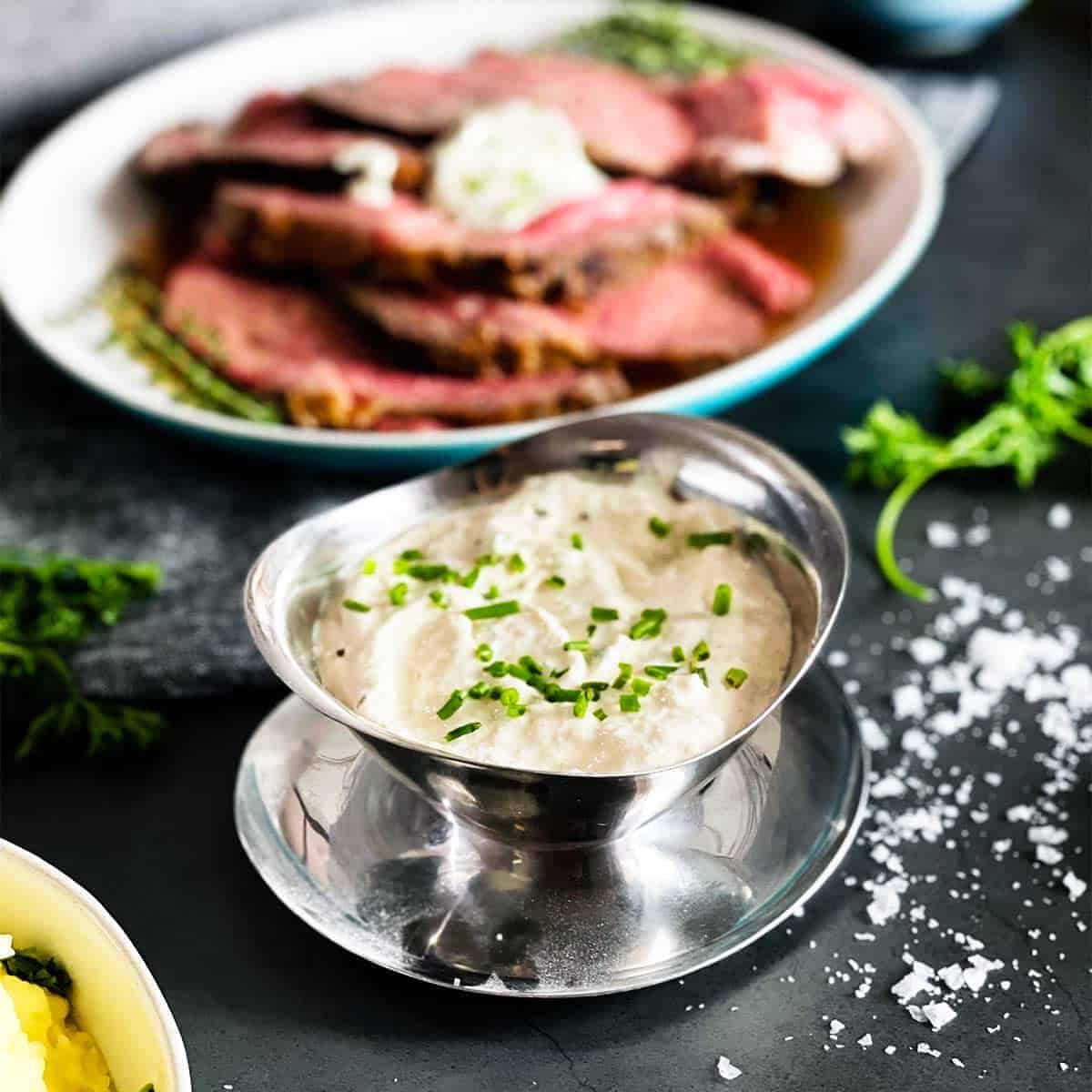 horseradish sauce in a silver bowl next to a platter of sliced prime rib