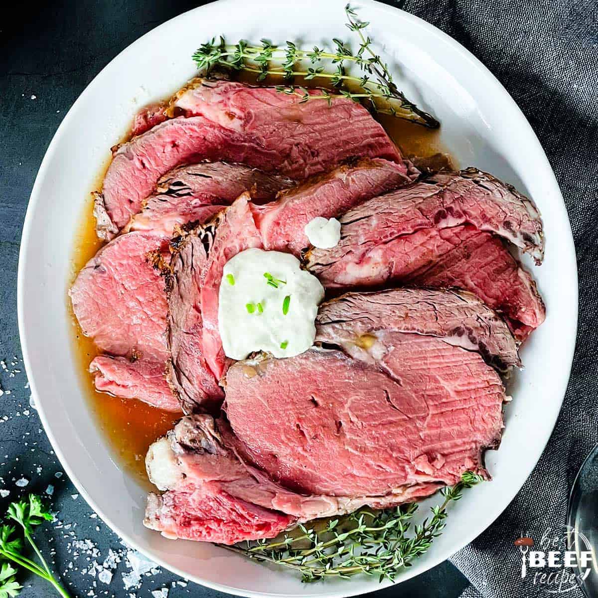 Horseradish sauce dolloped onto sliced prime rib on a white plate with herbs