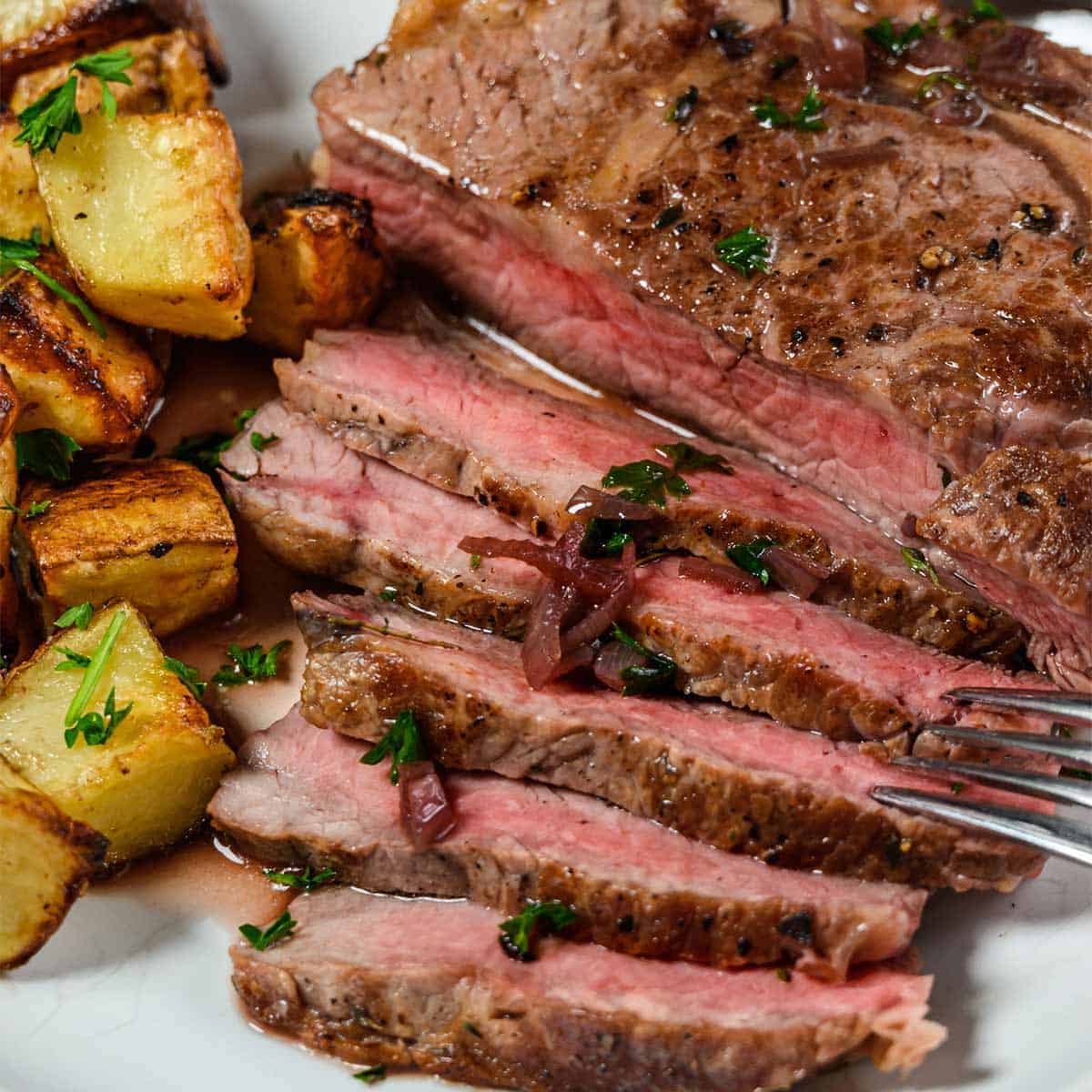 Sliced ribeye on a plate with potatoes up close