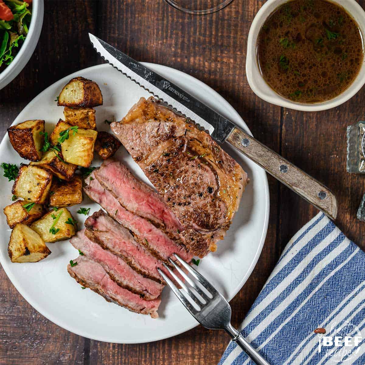 Steak sliced on a plate with red wine reduction sauce in a bowl