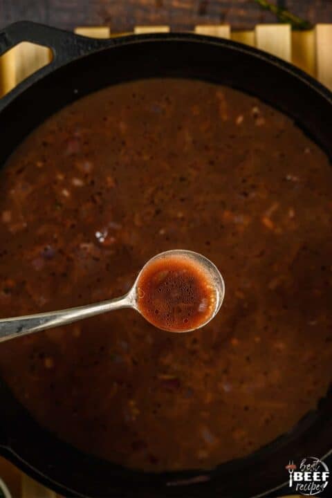 Completed red wine reduction sauce in pan with a spoon