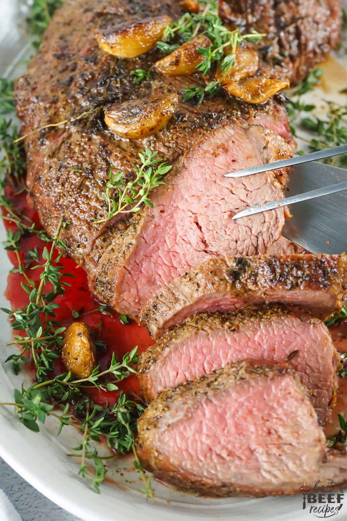 sliced smoked tri-tip steak on a platter with herbs