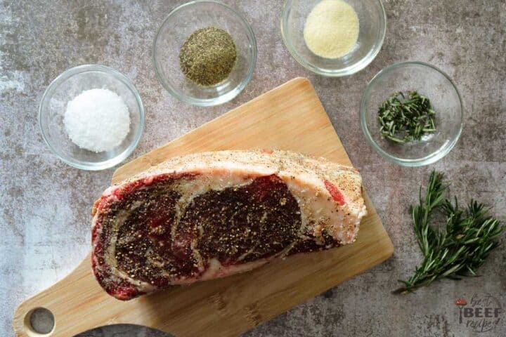 Seasoned prime rib roast on a cutting board next to bowls of seasonings