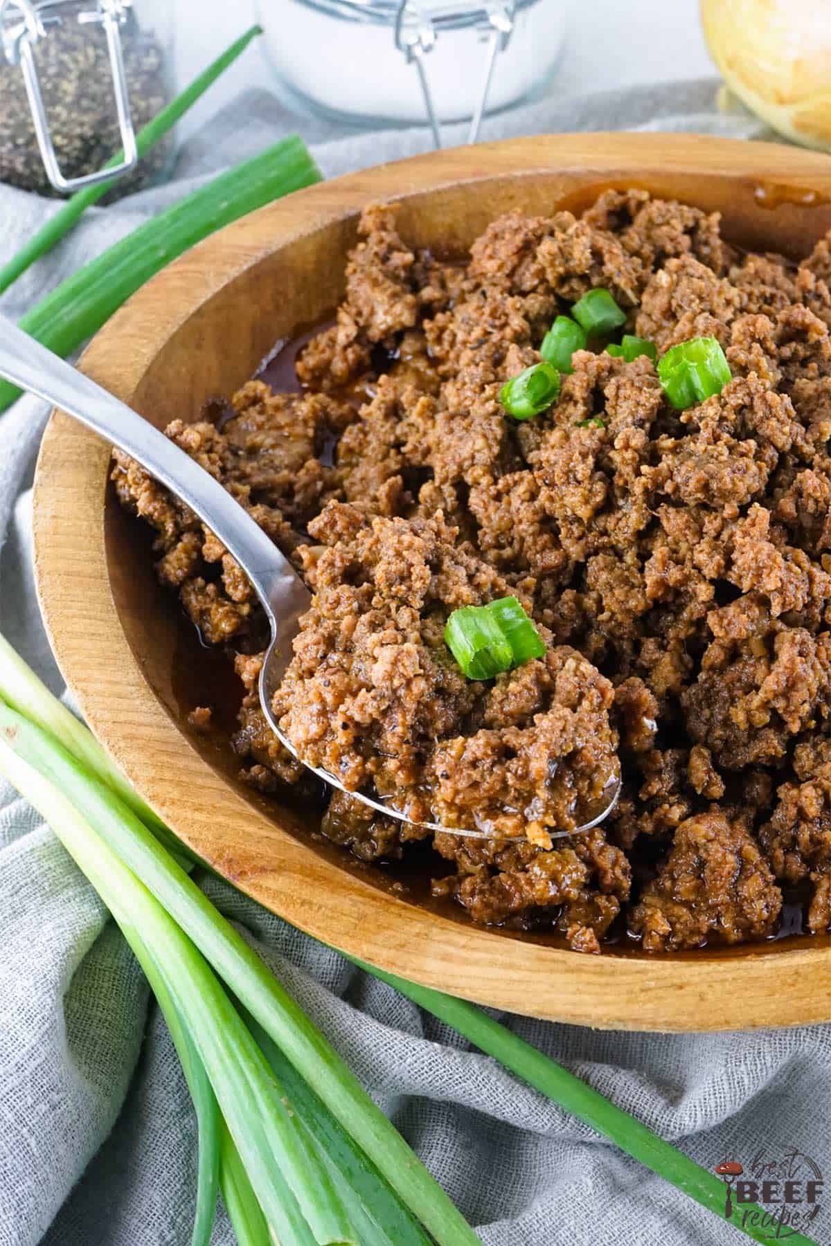 crockpot taco meat in a wooden bowl with a spoon and green onions on top