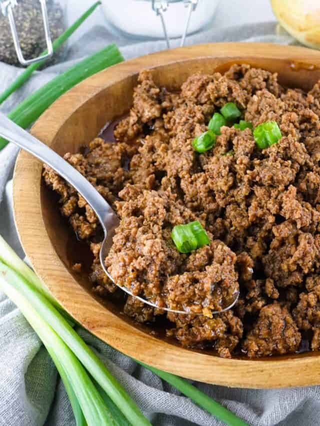 crockpot taco meat in a wooden bowl with a spoon and green onions on top