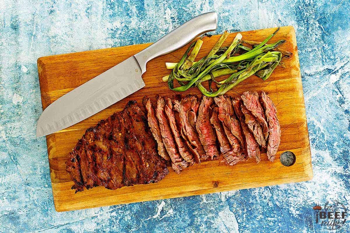 sliced steak on a cutting board with a knife and green onions