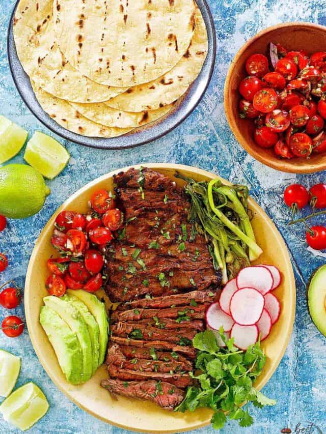 sliced carne asada beef on a plate with taco toppings