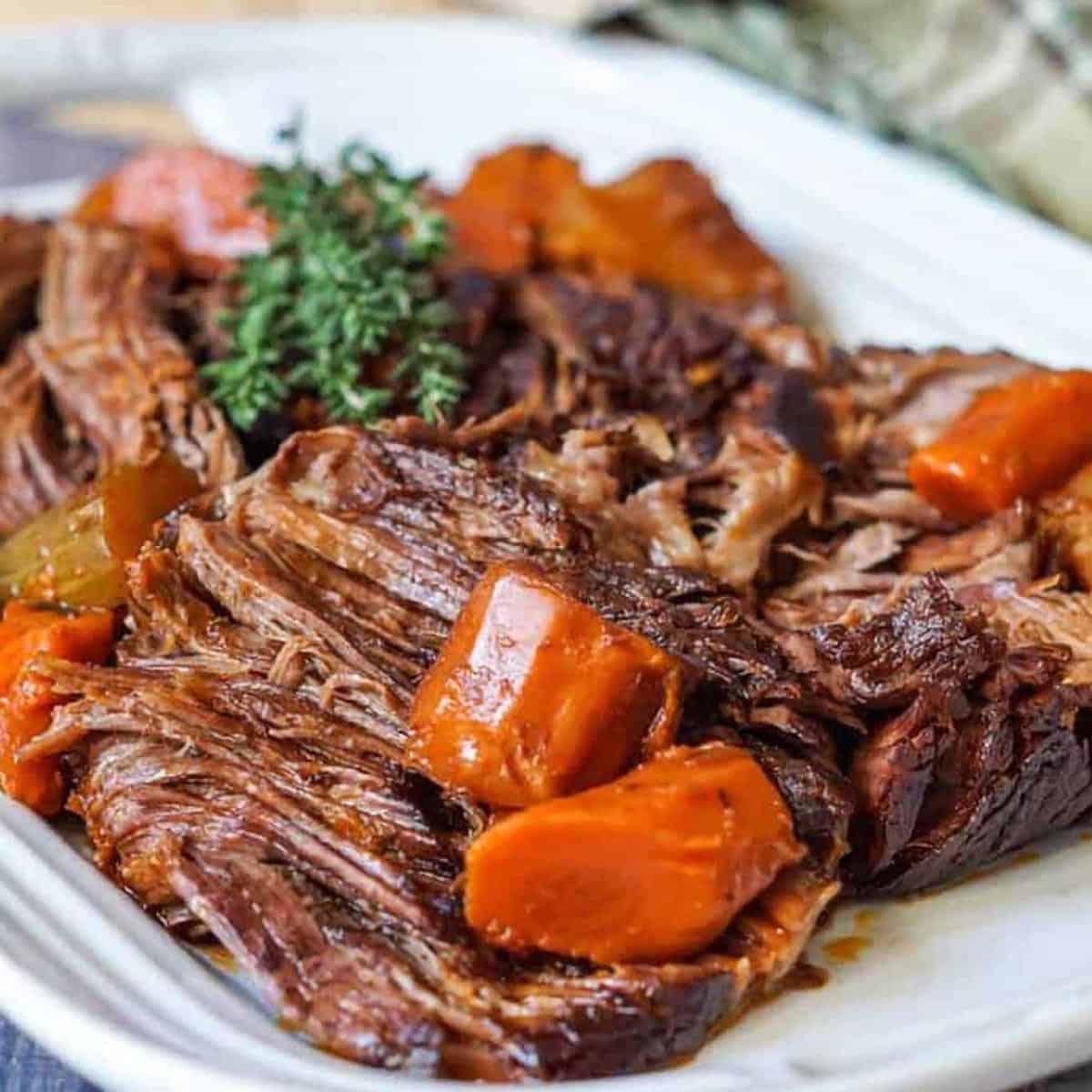 beef chuck roast on a white plate with herbs and carrots