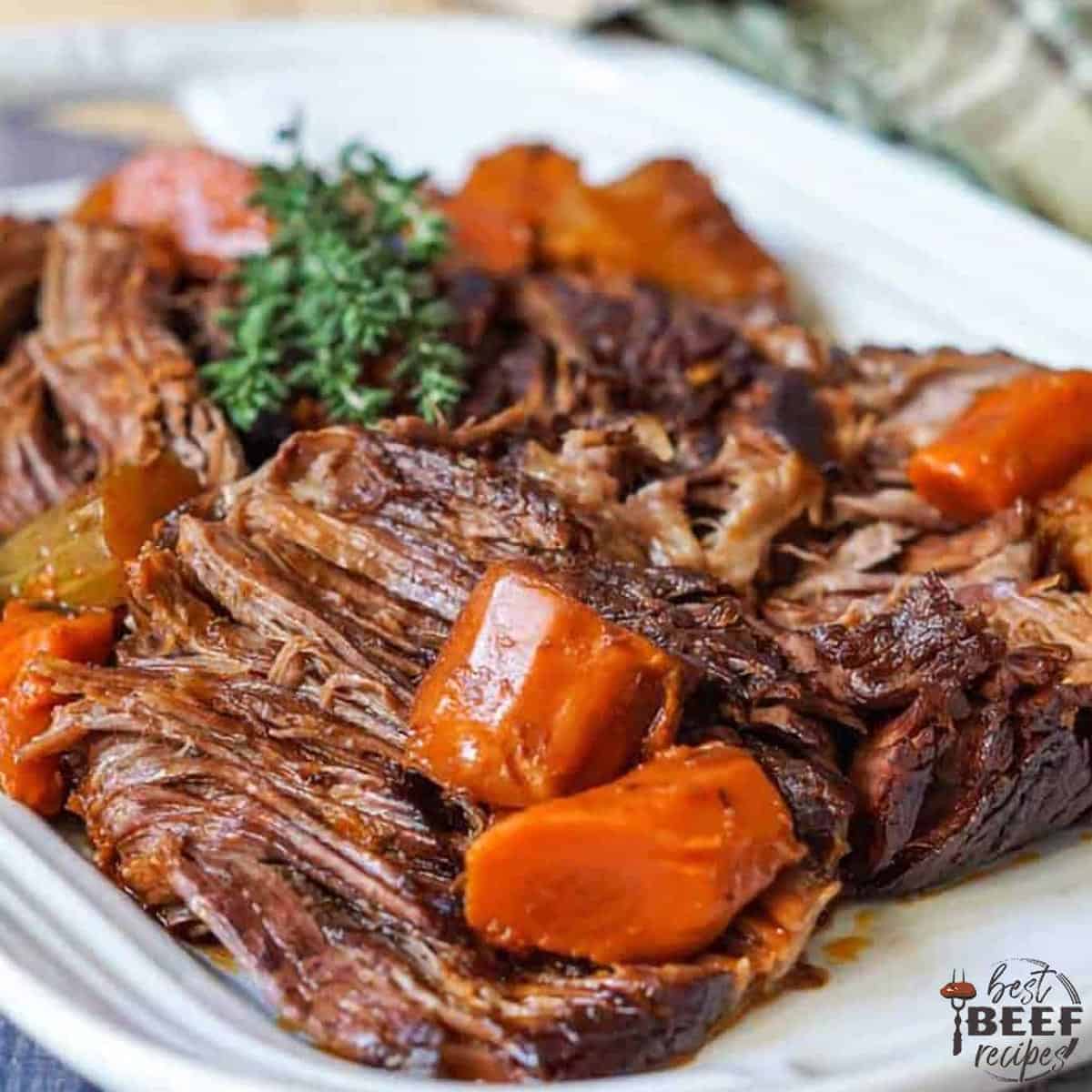 beef chuck roast on a white plate with herbs and carrots