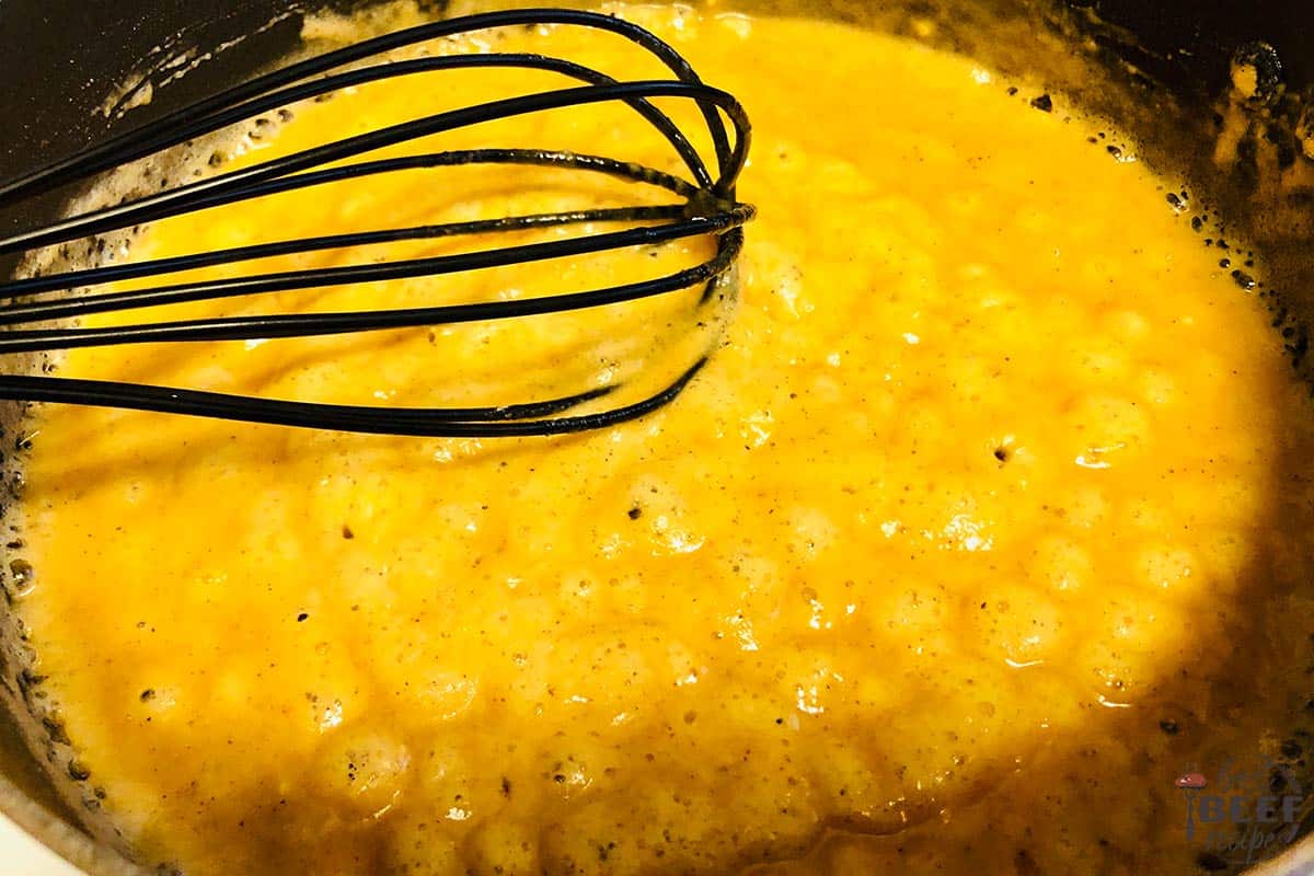 making cheese sauce for macaroni and cheese with a whisk and pan