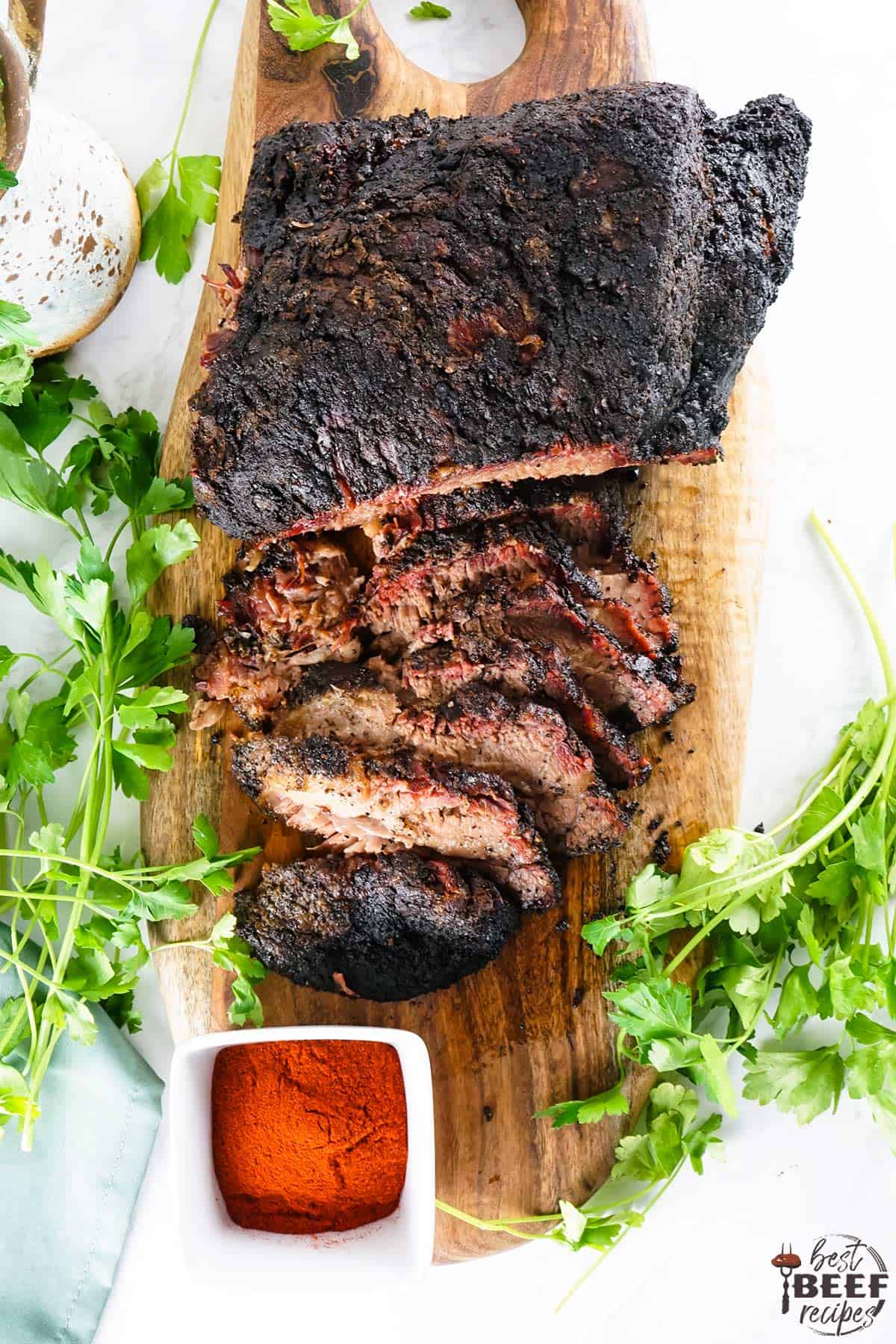 Sliced brisket on a serving board with a small bowl of brisket rub