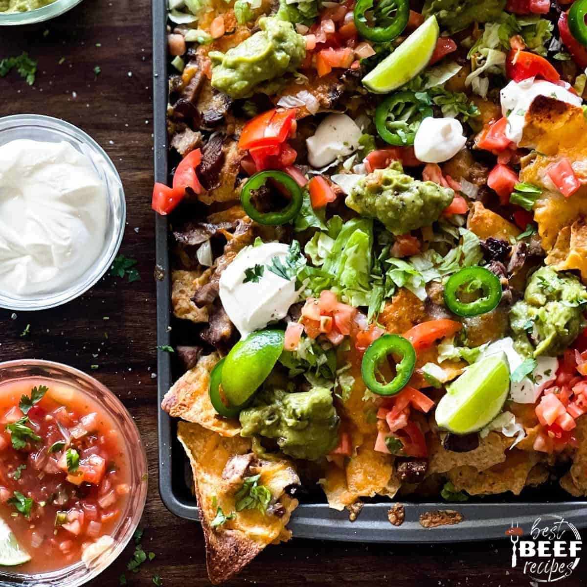 Steak nachos on a baking tray with toppings in bowls