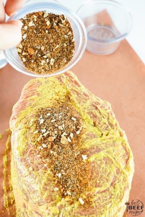 Pouring coffee rub onto prime rib with spicy brown mustard