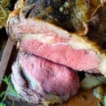 Sliced prime rib roast on a cutting board with herbs
