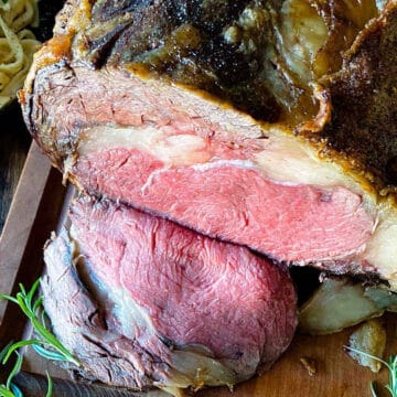 Sliced prime rib roast on a cutting board with herbs