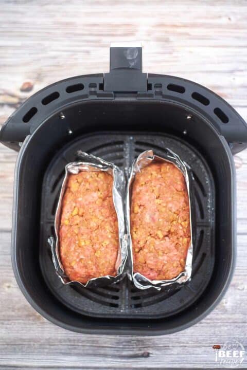 two meatloaves wrapped in aluminum foil in an air fryer