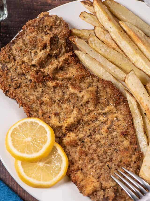 steak milanesa on a plate with lemon slices and fries