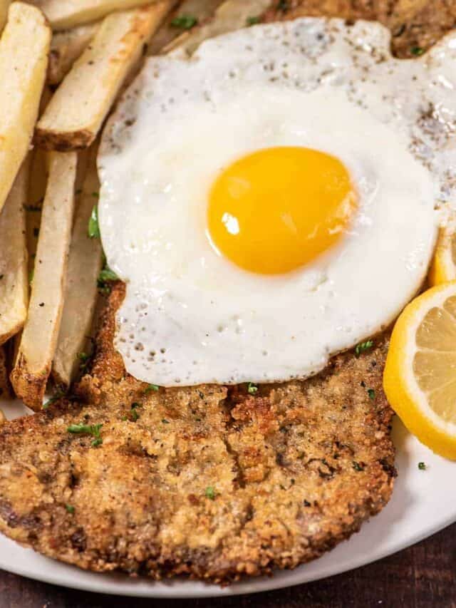 steak milanesa on a plate with an egg and fries