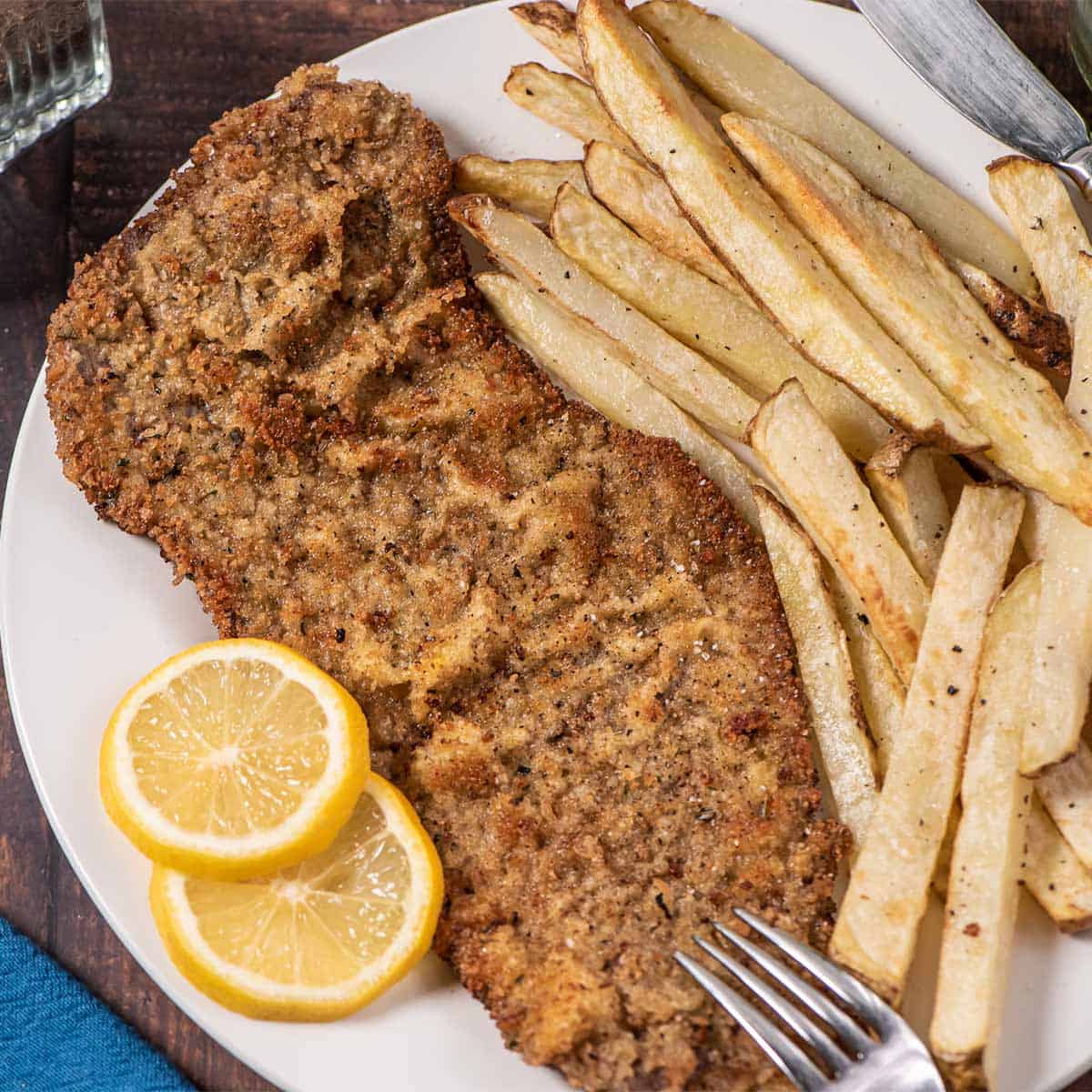 steak milanesa on a plate with lemon slices and fries