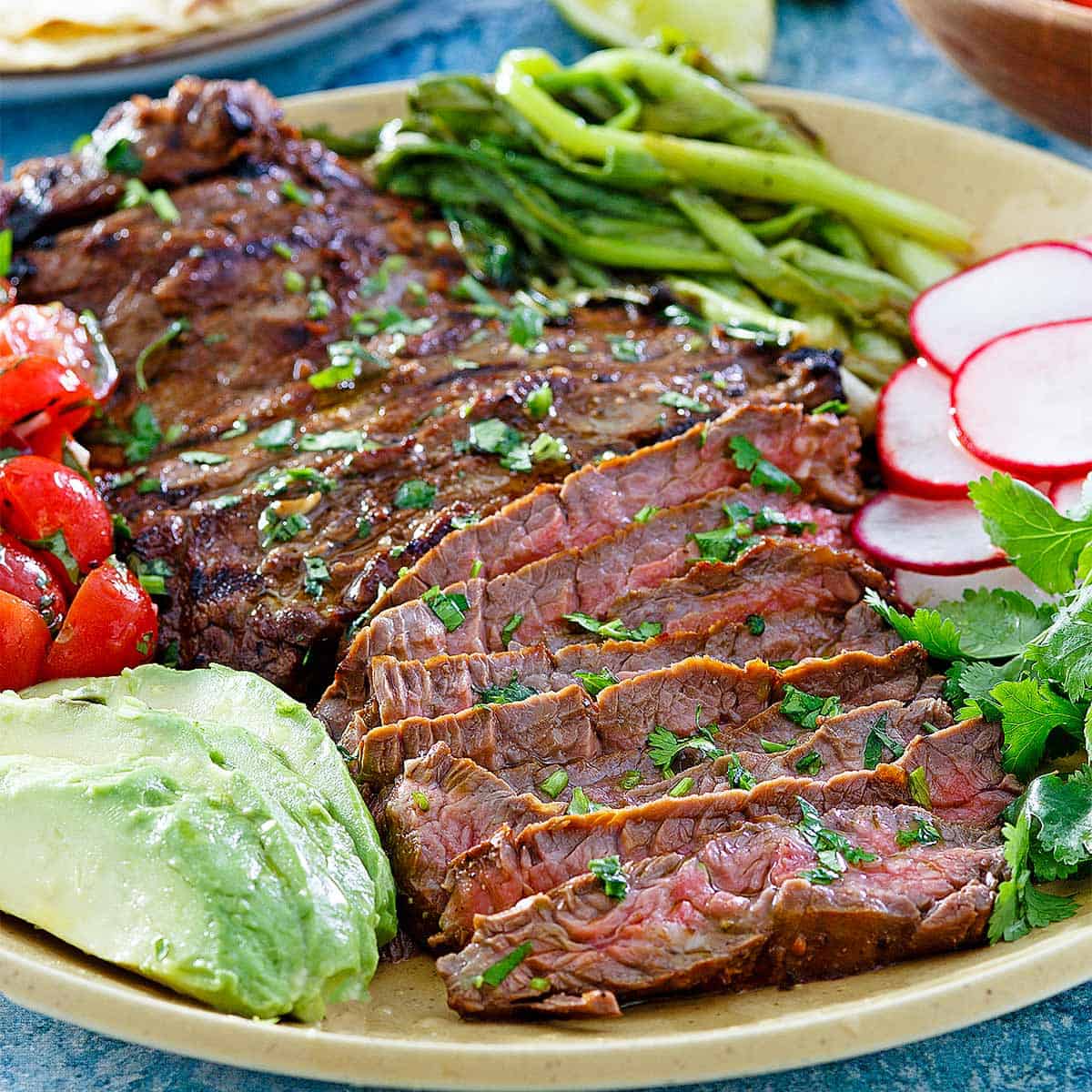 sliced carne asada on a plate with radishes avocados and tomatoes