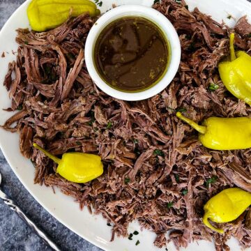 white plate of mississippi roast with au jus in a white bowl