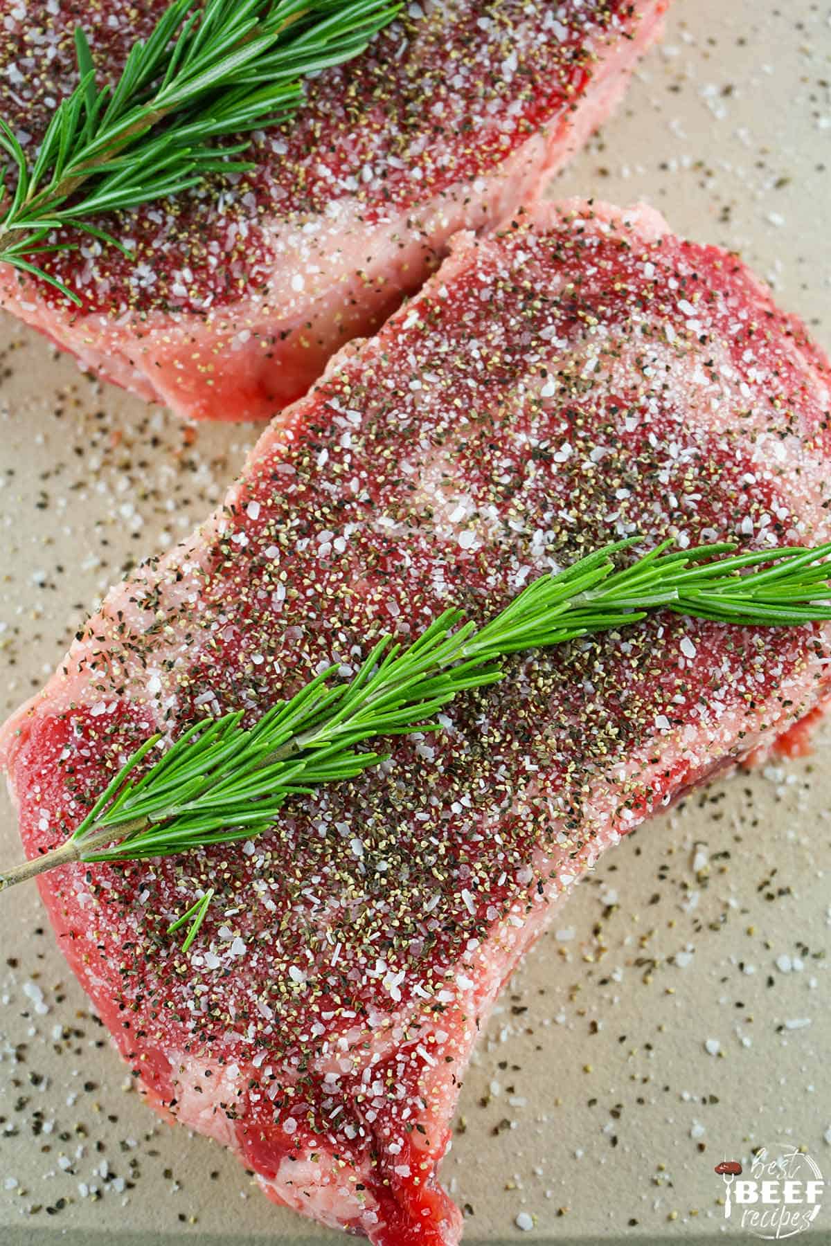 seasoned ribeye with a sprig of fresh rosemary on a counter