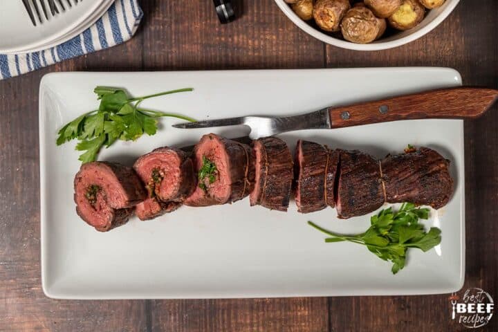 fresh parsley with beef roulade on a white platter with a steak fork