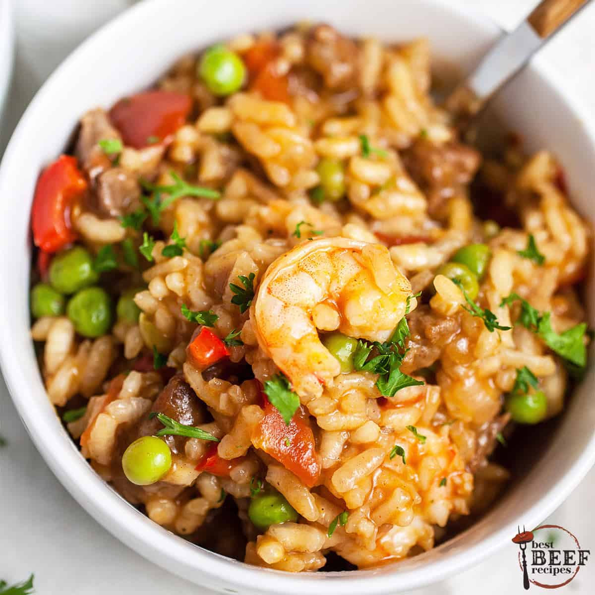 beef paella in a white bowl with shrimp and a fork