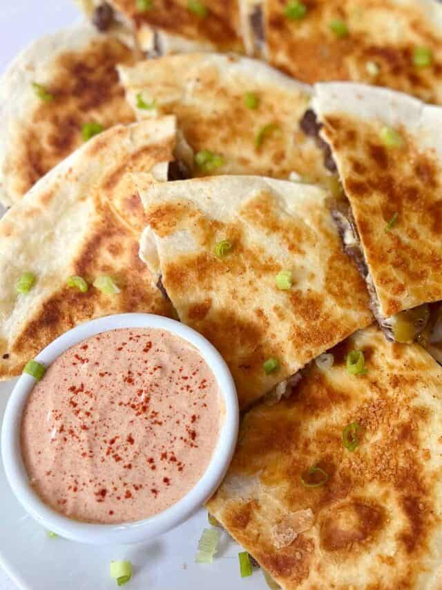 beef quesadilla slices on a plate with quesadilla sauce in a bowl