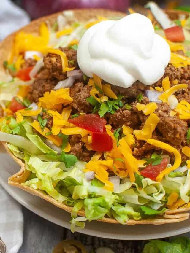 taco salad in a tortilla bowl on a white plate with a metal fork