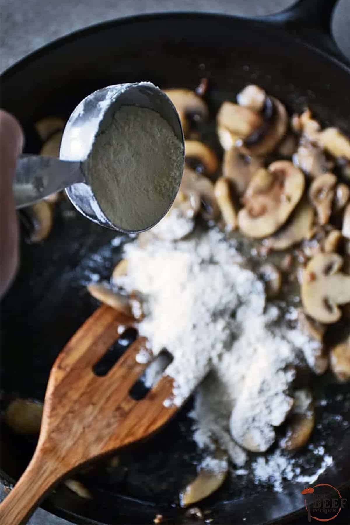 adding flour to pan with mushrooms