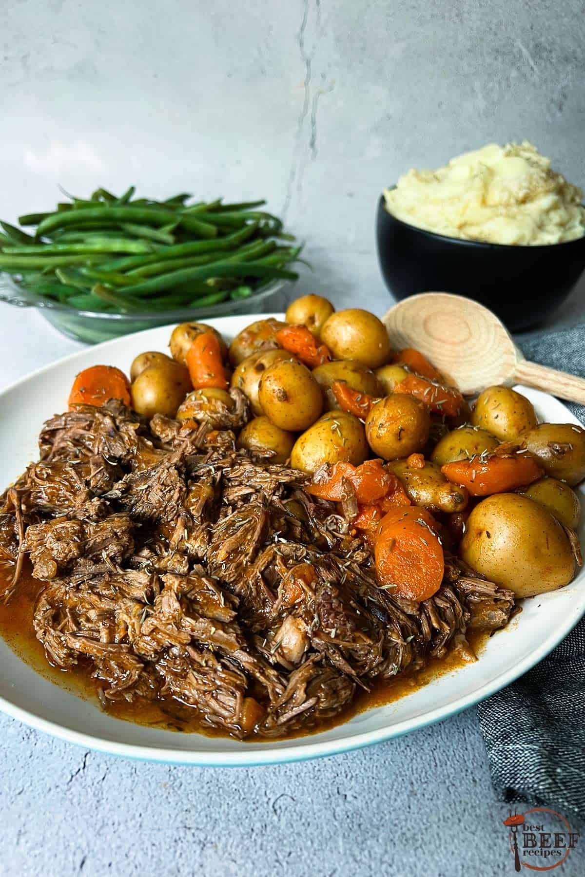 instant pot pot roast with a side of potatoes and carrots on a white plate with a wooden spoon