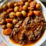 instant pot pot roast on a white plate covered with gravy and next to carrots and potatoes