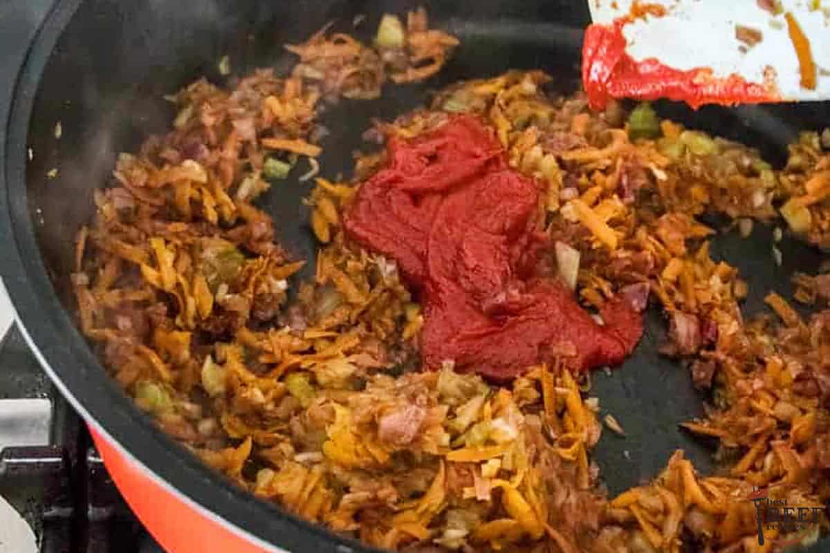 adding tomato paste into a pan