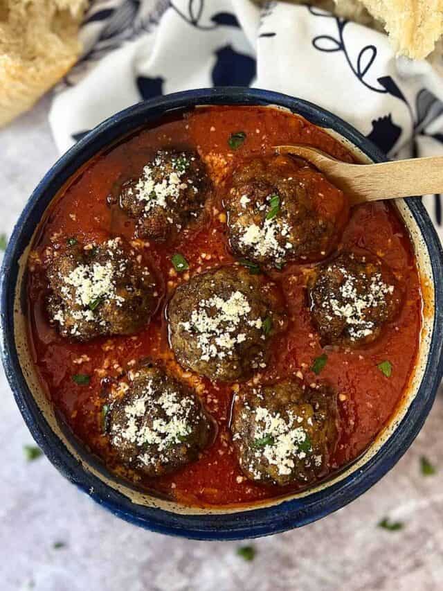 italian meatballs in red sauce in a blue bowl with a wood spoon and bread on the side.
