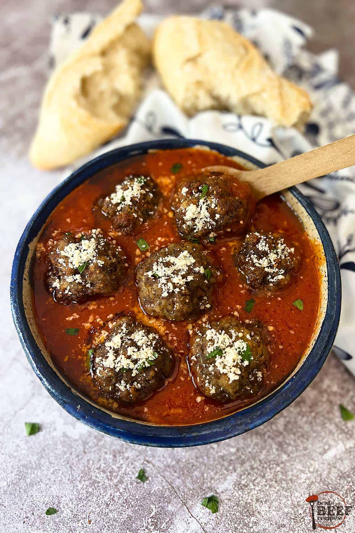 italian meatballs in red sauce in a blue bowl with a wood spoon and bread on the side.