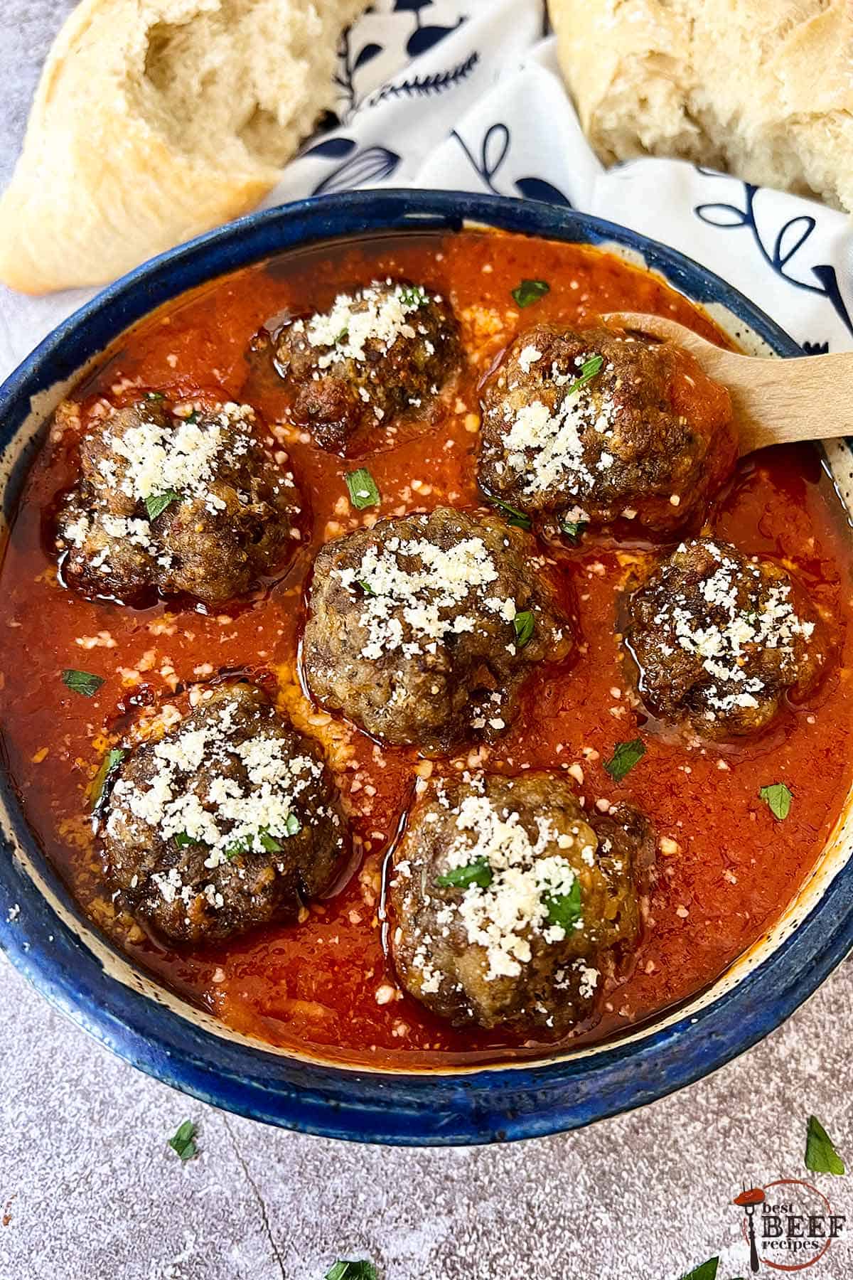 italian meatballs in red sauce in a blue bowl with a wood spoon and bread on the side.