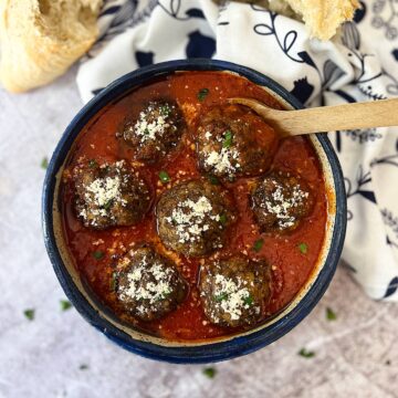 italian meatballs in red sauce in a blue bowl with a wood spoon and bread on the side.