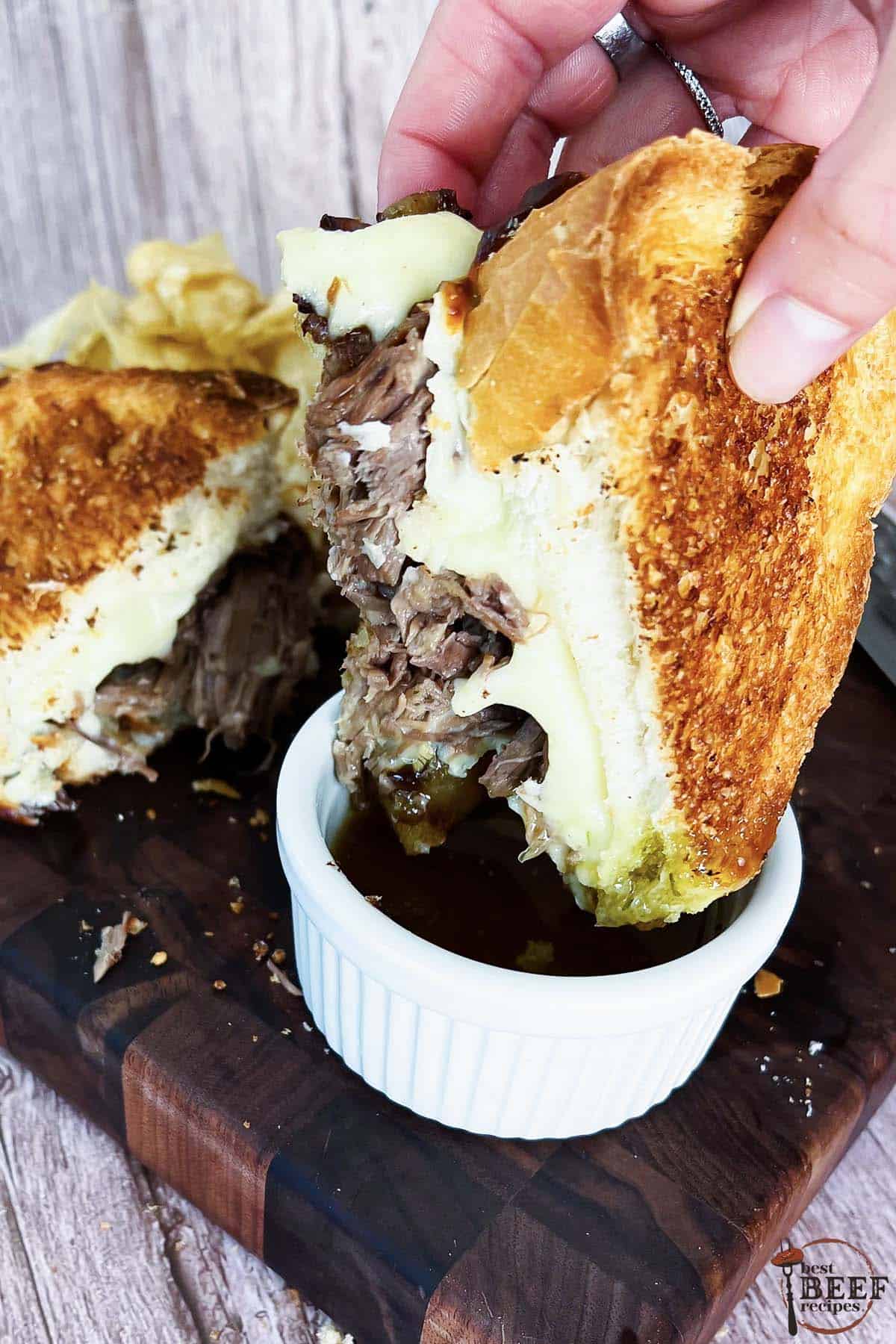dipping a pot roast sandwich in a cup of au jus