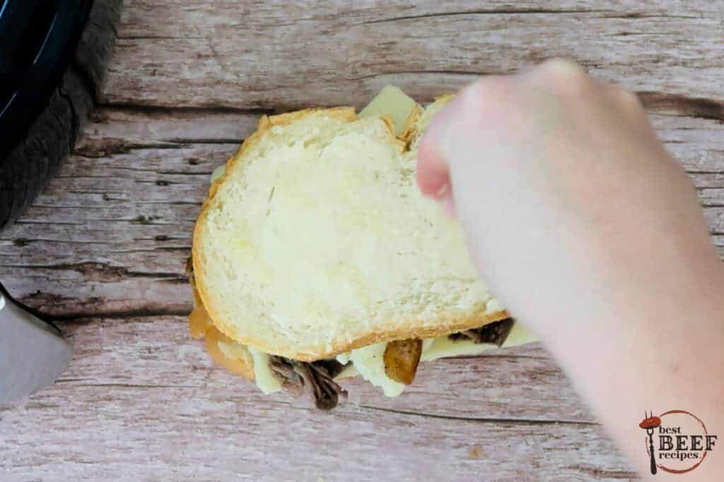 topping pot roast sandwich with another piece of bread topped with butter and parmesan cheese