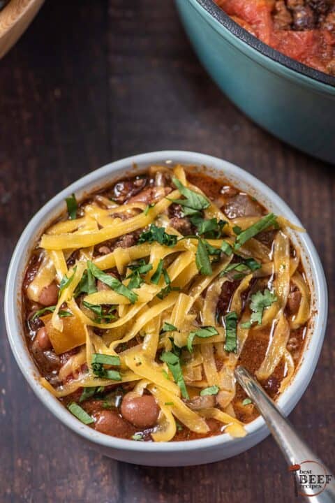 beef chili up close in a bowl with a spoon, topped with cheese