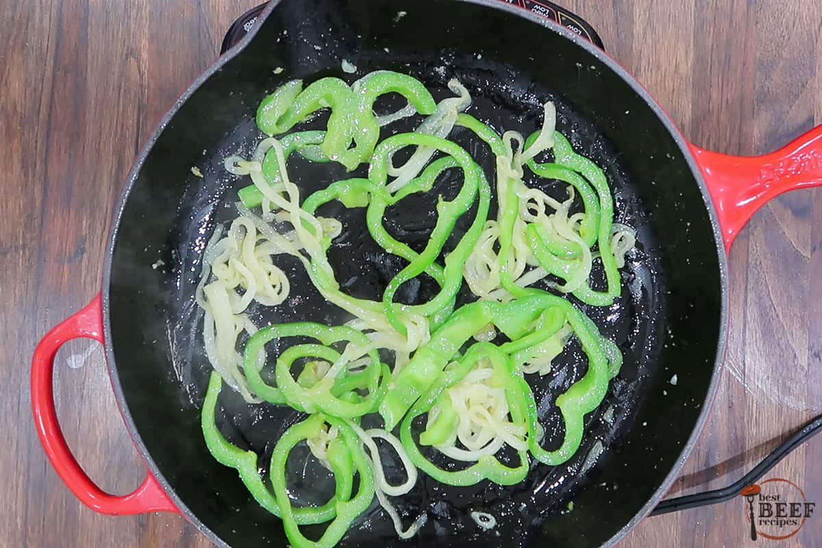 Bell peppers, onions, and garlic cooking in oil in a skillet