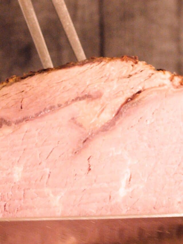 A finished prime rib being sliced with a knife and meat fork on a brown background